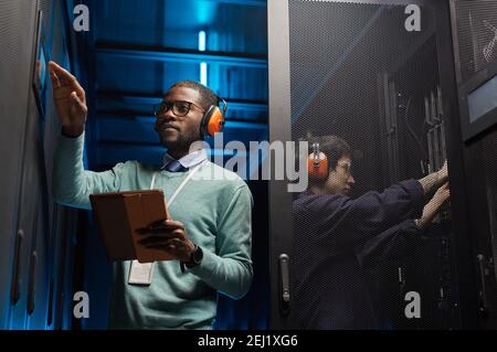 Waist up portrait of two technicians setting up computer network while working in data center Stock Photo