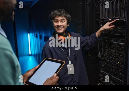 Waist up portrait of smiling Asian man looking at colleague while setting up supercomputer servers in data center, copy space Stock Photo