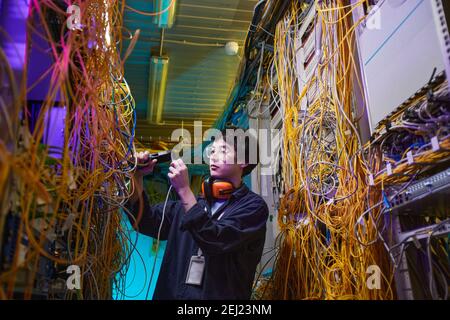 Waist up portrait of young network technician connecting cables in server room, copy space Stock Photo