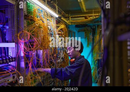Side view portrait of young network technician connecting cables in server room, copy space Stock Photo