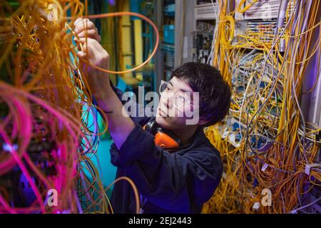 High angle portrait of young network technician connecting cables in server room, copy space Stock Photo