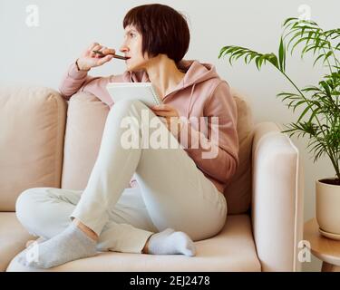 Mature female writing on to-do list notepad, mental health journaling, self-reflection Stock Photo