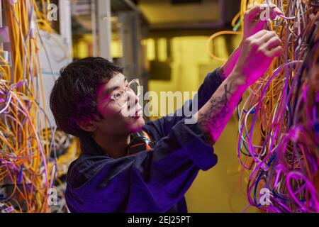 Side view portrait of young network technician connecting wires and cables in server room Stock Photo