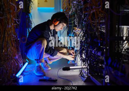 Full length portrait of young network technician connecting cables and wires while setting up internet connection in server room, copy space Stock Photo