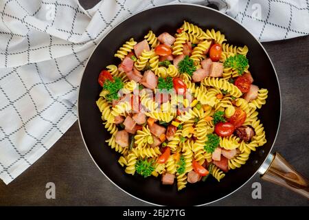 Colorful pasta rotini, cherry tomatoes and ham on pan. Close up. Top view. Stock Photo