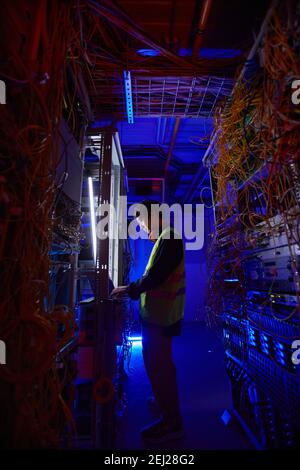 Futuristic side view at young network technician using laptop in server room while setting up internet connection Stock Photo