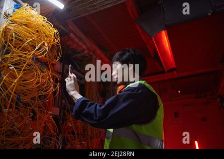Low angle portrait of young network technician taking photos in server room while inspecting equipment Stock Photo