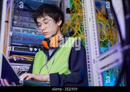 Low angle portrait of young network technician using laptop in server room while setting up internet connection, copy space Stock Photo