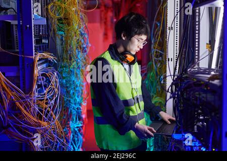 Side view portrait of young network technician using laptop in server room while setting up internet connection, copy space Stock Photo