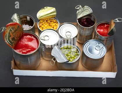 Caned vegetables such as beans, peas, corn, tomatos in cardboard box. Tin cans. Dark background Stock Photo