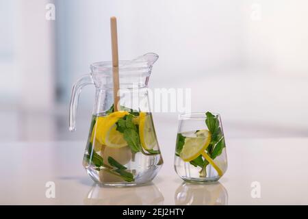 A jar and a glass with lemon slices, mint leaves and a wooden spoon on an out of focus background. Close up. Healthy refreshment concept. Stock Photo