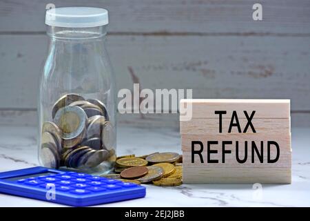 Glass jars with blurred multicurrency coins, calculator and text on white torn paper - Tax refund Stock Photo