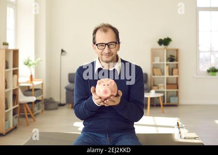 Portrait of happy middle-aged man holding piggy bank, smiling and looking at camera Stock Photo