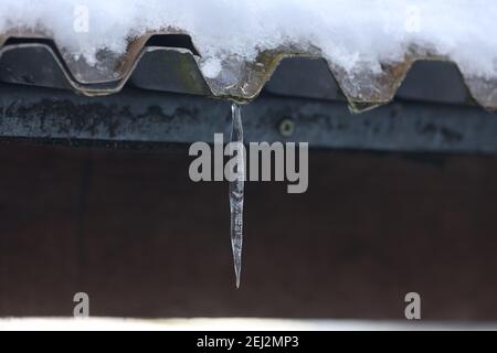 The snow on the roof melts and forms ice icicles. Stock Photo