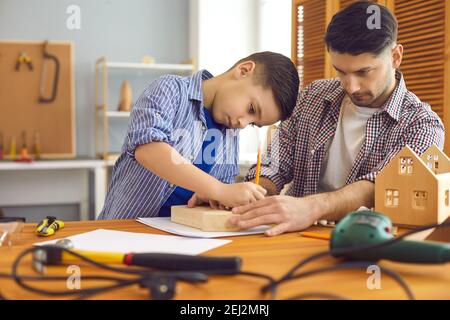 Little boy and his father making wooden house models as part of school DIY project Stock Photo