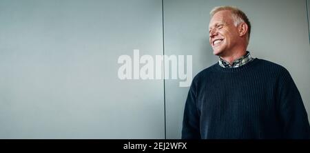 Wide angle shot of a senior businessman looking away and smiling. Positive senior male professional in office. Stock Photo