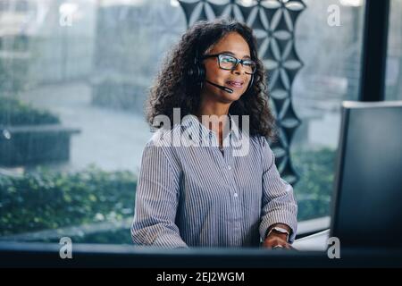 Mature business woman talking on headset while working at her desk. Female call center executive at work. Stock Photo