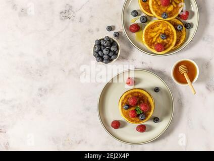 Two plates with tasty american pancakes with raspberries, blueberries, and honey. Top view, marble table. Stock Photo