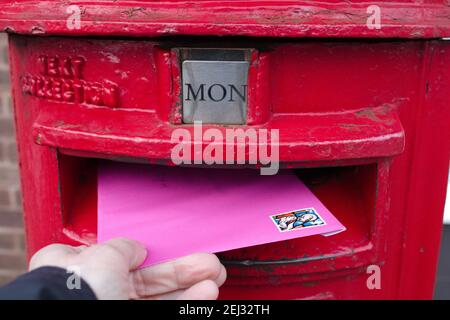 Posting a letter in a post box concept, UK post box and pink envelope Stock Photo