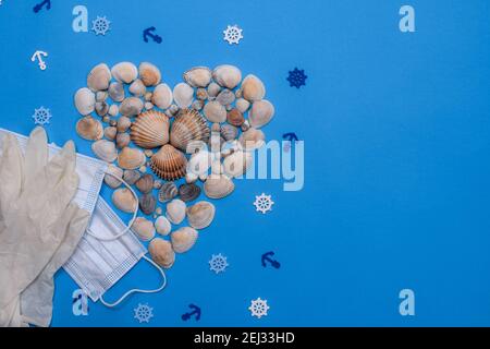 Summer composition shells form of heart with a medical mask and gloves on a blue background. top view. copy space Stock Photo