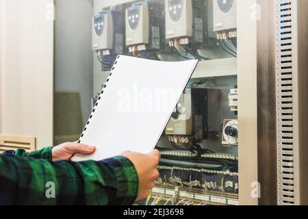 Man wearing a green checkered shirt doing the maintenance of electronic meters holding a checking notebook Stock Photo