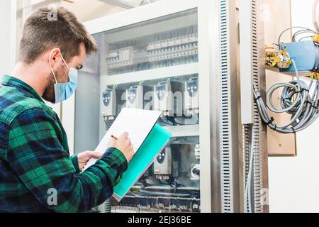 Young engineer taking notes on a notebook and doing the maintenance of a control panel Stock Photo