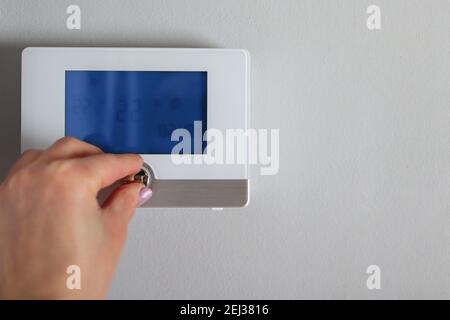 Female hand adjusts and regulates the room temperature on the smart switch on the wall at home. Copy space for text. Smart house concept Stock Photo