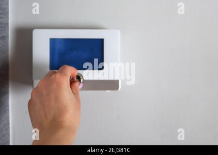 Hand adjusts and regulates the room temperature on the smart switch with a digital display on the wall at home. Smart house concept Stock Photo