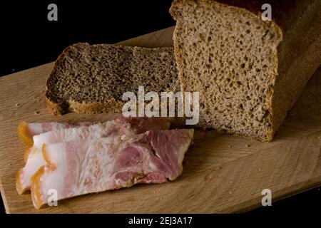 Black bread and salted lard with strips of meat on a wooden board on a black background Stock Photo