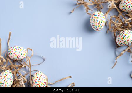 Happy Easter card. Frame made of colorful Easter eggs and straw on blue background. Flat lay, top view. Stock Photo