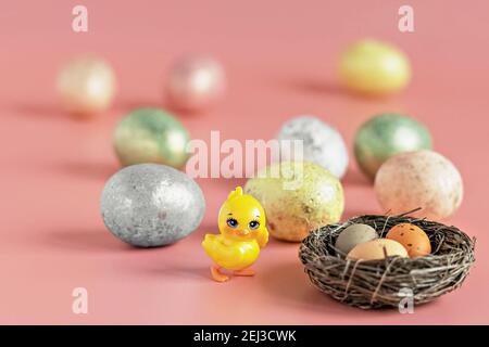 Easter eggs in a natural nest with bird eggs. Painted eggs and a decorative chicken on a pink background of pastel colors. Selective focus. Stock Photo