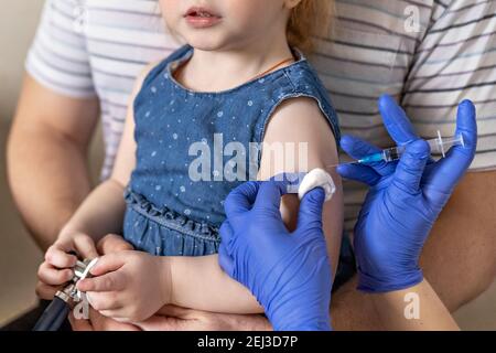 A little girl with her father in the doctor's office at the clinic is being vaccinated against the coronavirus.The concept of vaccination, immunizatio Stock Photo