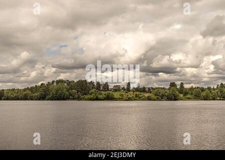 Cottage village on the shore of the lake at sunset before the rain. The clouds are thunderous in the sky. Landscape. Stock Photo