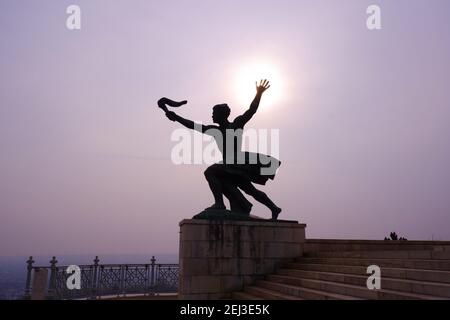 Budapest, Hungary - February 18, 2021: statue of a man holding a torch on Gellert Hill citadel in the misty city Stock Photo