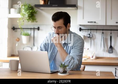 Pensive young man work on laptop at home kitchen Stock Photo