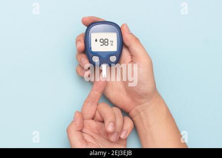 Man using glucometer, checking blood sugar level. Diabetes concept on blue background Stock Photo