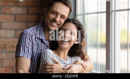 Head shot portrait overjoyed young couple hugging, standing at home Stock Photo