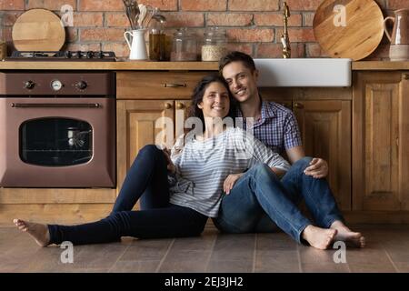 Portrait smiling man and woman sitting on warm wooden floor Stock Photo