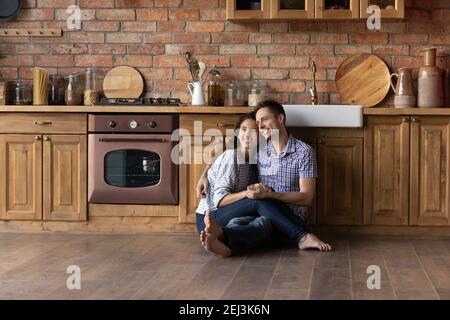 Smiling dreamy man and woman hugging, sitting on floor Stock Photo
