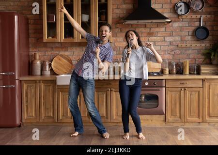 Overjoyed man and woman having fun, singing in utensils Stock Photo