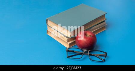a stack of books, red apple and glasses isolated on colorful surface, simple abstract study concept Stock Photo