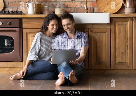 Happy woman and man using laptop, sitting on warm floor Stock Photo