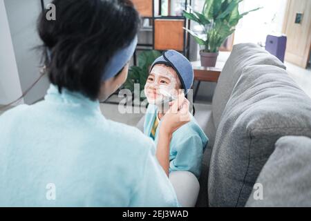 smiling little girl face when a mother smears facial cream with a brush on her face Stock Photo