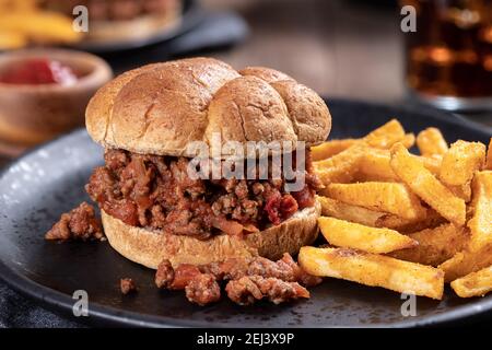 Closeup of a sloppy joe sandwich and french fries on a black plate Stock Photo