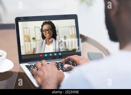 Black Man Using Laptop In Cafe For Online Meeting With Female Colleague Stock Photo