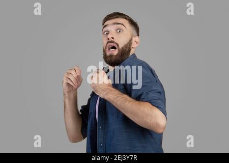 Young hipster guy being scared or terrified over grey studio background. Negative human emotions and feelings concept Stock Photo