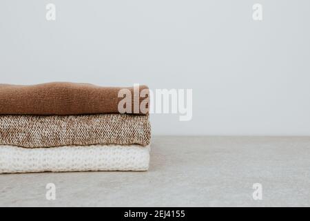 Women fashion composition. Warm winter female woollen knitted sweaters, pullovers stack on white background. Modern clothes concept for magazine. Stock Photo