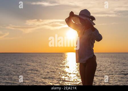 Silhouette of young happy carefree woman posing with hat on the beach at sunset Stock Photo