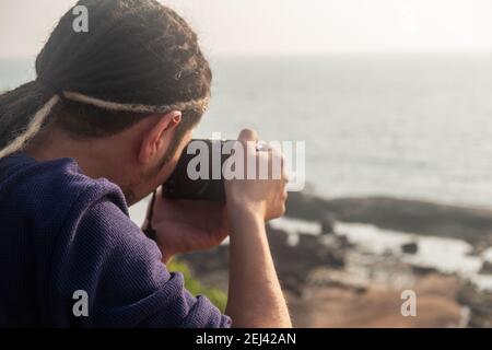 Young Asian photographer taking a picture from the top of a mountain, Northern Goa, India Stock Photo