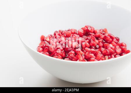 Close up detail of superfood pomegranate seeds in a white bowl on a plain white surface and background. Stock Photo